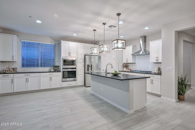 kitchen featuring stainless steel appliances, white cabinetry, pendant lighting, and wall chimney range hood