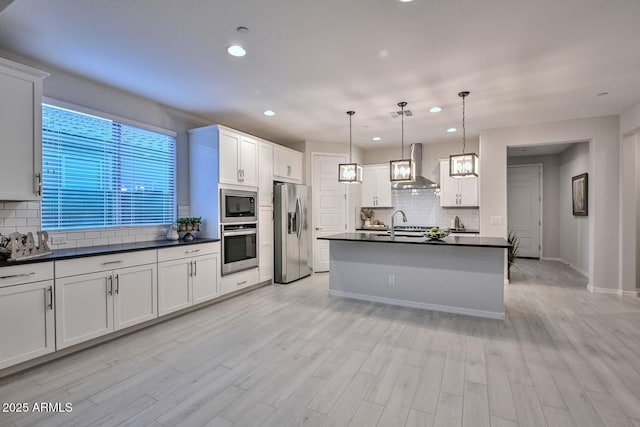 kitchen with stainless steel refrigerator with ice dispenser, built in microwave, wall chimney exhaust hood, white cabinetry, and decorative light fixtures