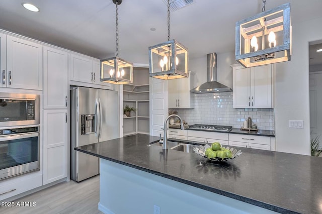 kitchen featuring appliances with stainless steel finishes, pendant lighting, sink, white cabinets, and wall chimney range hood