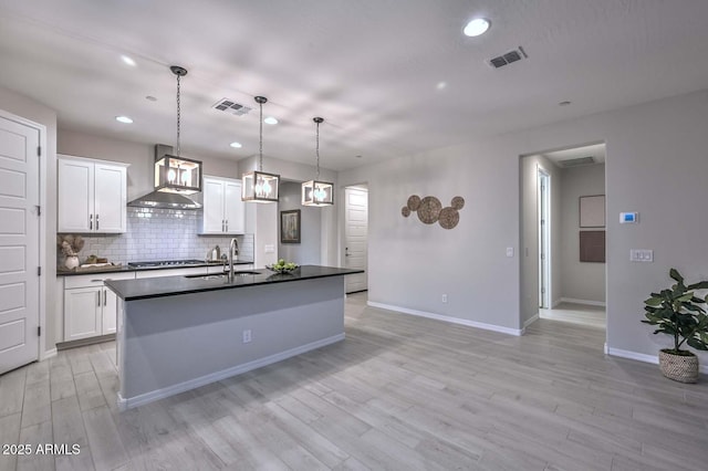 kitchen featuring pendant lighting, sink, white cabinetry, and wall chimney exhaust hood