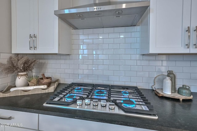 interior details with stainless steel gas cooktop, white cabinets, backsplash, and wall chimney exhaust hood