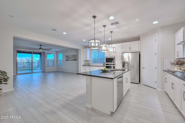 kitchen with tasteful backsplash, decorative light fixtures, appliances with stainless steel finishes, a kitchen island with sink, and white cabinets