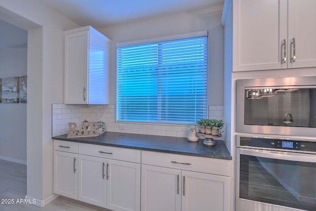 kitchen featuring tasteful backsplash, stainless steel microwave, and white cabinets