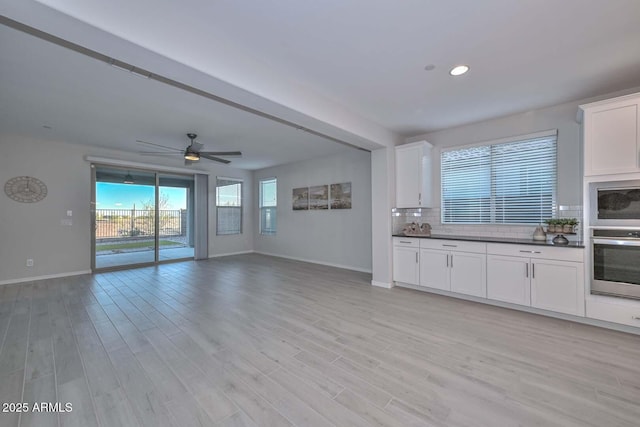 kitchen with appliances with stainless steel finishes, tasteful backsplash, white cabinetry, ceiling fan, and light hardwood / wood-style flooring