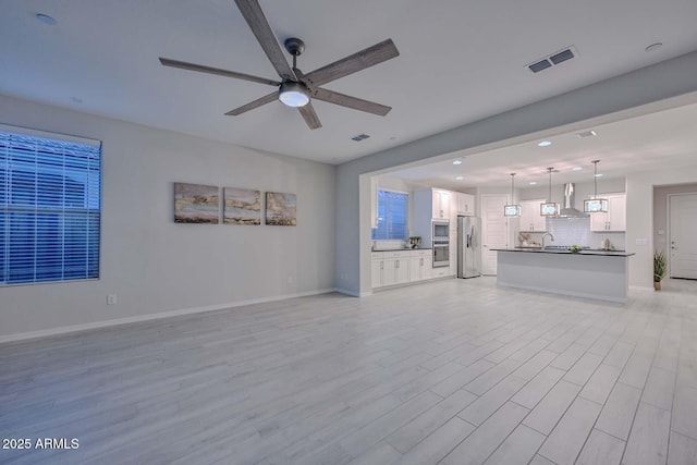 unfurnished living room with sink, ceiling fan, and light wood-type flooring