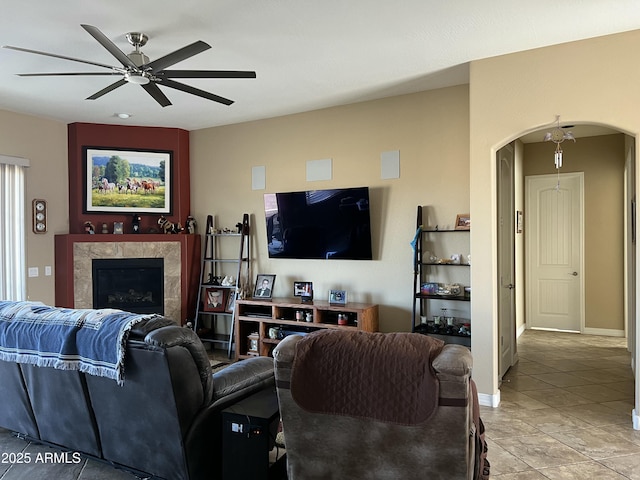 living area featuring a ceiling fan, arched walkways, baseboards, and a tile fireplace