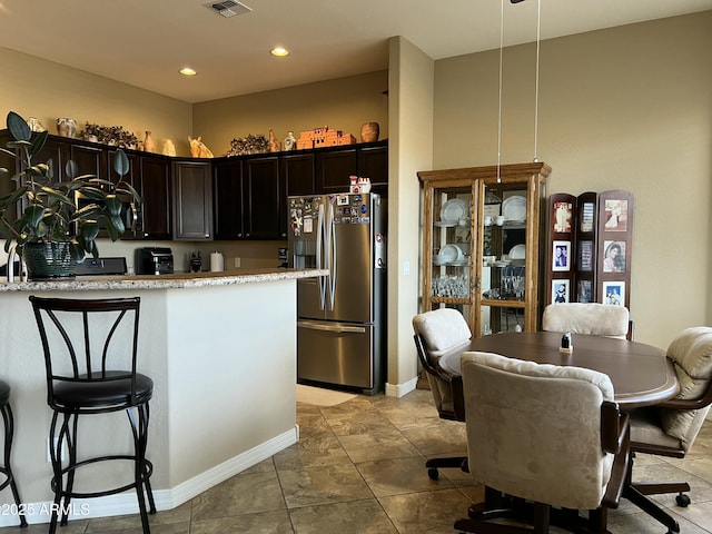 kitchen featuring dark brown cabinetry, visible vents, light stone counters, freestanding refrigerator, and recessed lighting