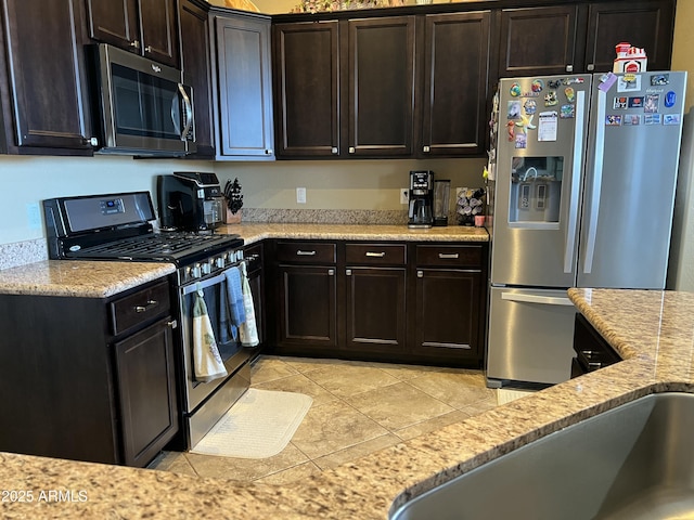 kitchen with light tile patterned floors, appliances with stainless steel finishes, dark brown cabinetry, and light stone countertops