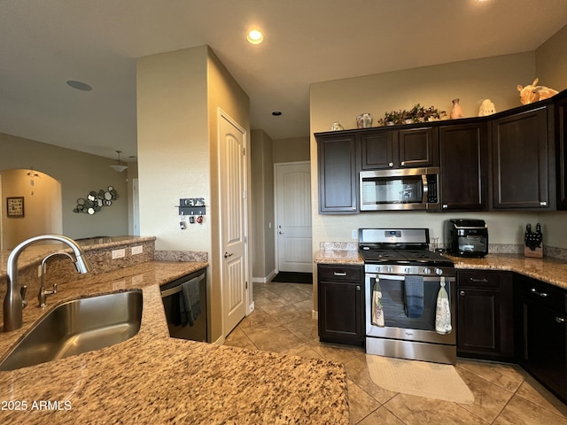 kitchen featuring appliances with stainless steel finishes, arched walkways, a sink, and light stone countertops