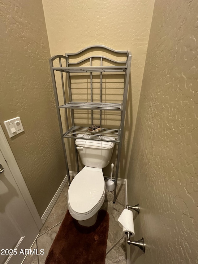 bathroom featuring a textured wall, tile patterned flooring, toilet, and baseboards