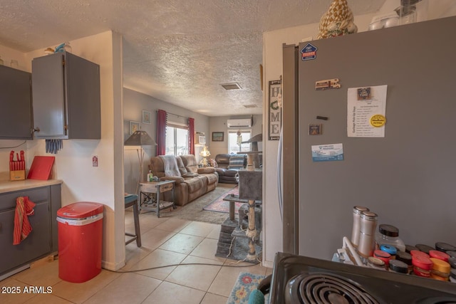 interior space with a wall mounted air conditioner, stainless steel fridge, a textured ceiling, and light tile patterned floors