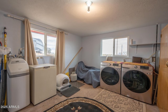 clothes washing area with separate washer and dryer, a wealth of natural light, and a textured ceiling