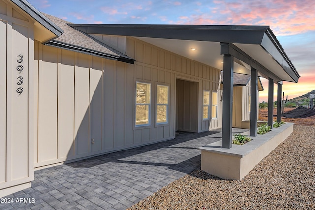 3939 S Veronica Ln, Gold Canyon, AZ 85118 - exterior entry at dusk featuring a shingled roof, board and batten siding, and a patio area