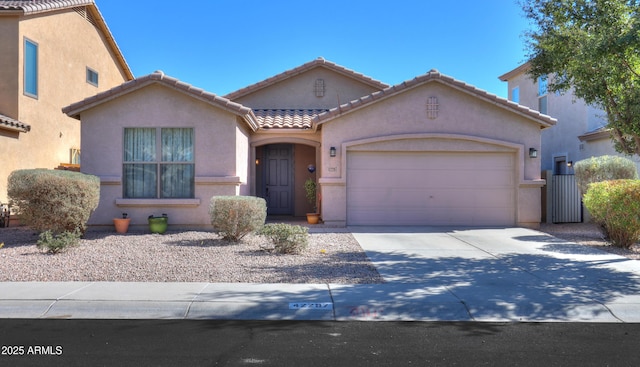 mediterranean / spanish house with a garage, a tile roof, concrete driveway, and stucco siding