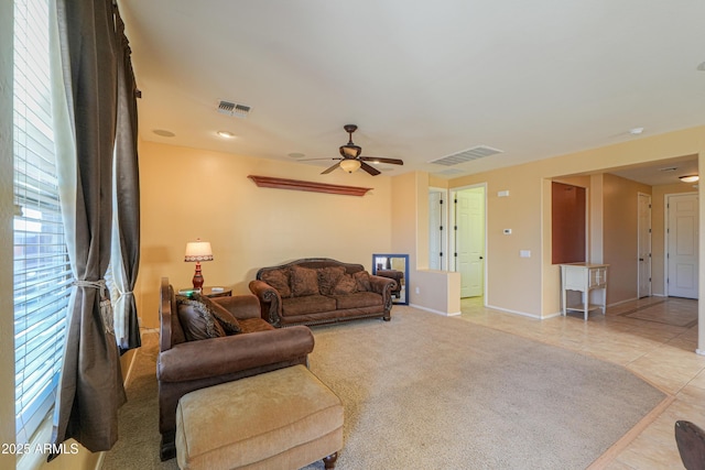 living room featuring light tile patterned flooring, ceiling fan, visible vents, and light colored carpet