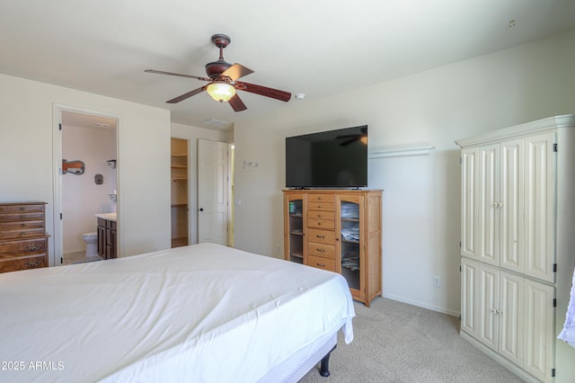 bedroom with ceiling fan, connected bathroom, light carpet, baseboards, and a spacious closet