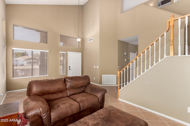 tiled living room featuring baseboards, visible vents, stairs, and a towering ceiling