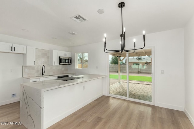 kitchen with sink, kitchen peninsula, pendant lighting, light stone countertops, and white cabinets