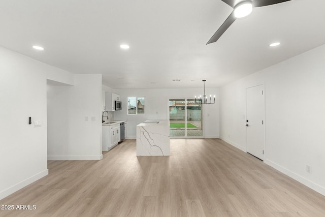 unfurnished living room with sink, ceiling fan with notable chandelier, and light hardwood / wood-style floors