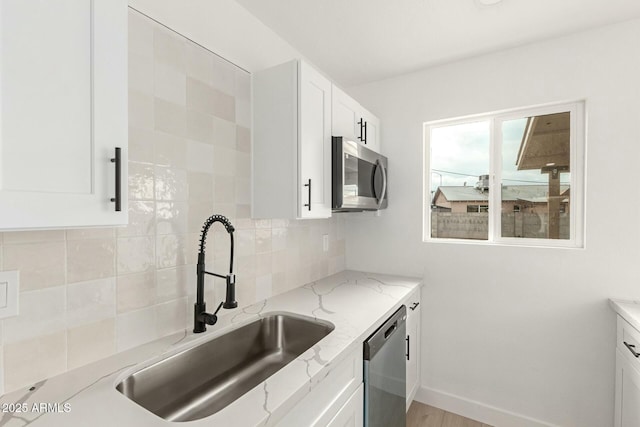 kitchen featuring appliances with stainless steel finishes, white cabinetry, sink, decorative backsplash, and light stone countertops