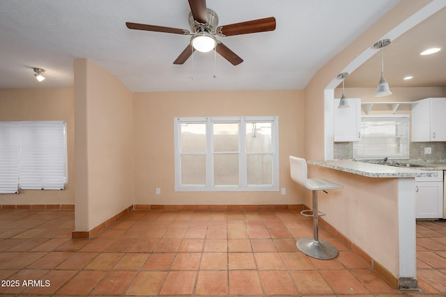 kitchen with a breakfast bar area, white cabinetry, light stone counters, hanging light fixtures, and backsplash