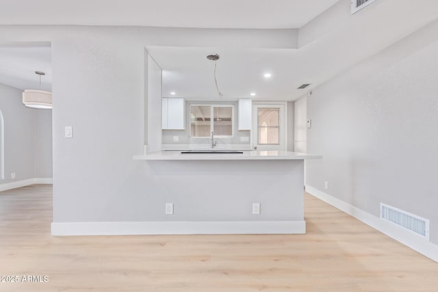 kitchen featuring white cabinetry, kitchen peninsula, light hardwood / wood-style floors, and decorative light fixtures