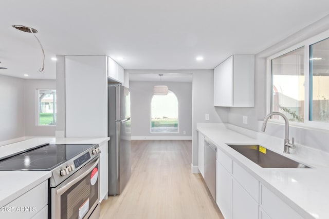 kitchen with decorative light fixtures, sink, white cabinets, stainless steel appliances, and light wood-type flooring