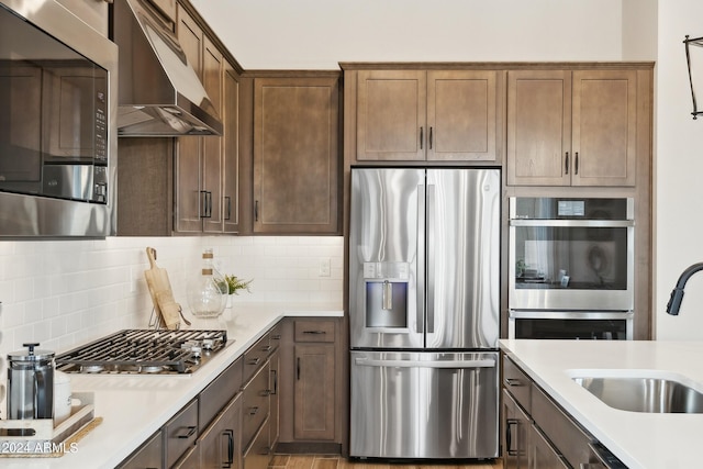 kitchen with decorative backsplash, stainless steel appliances, light countertops, under cabinet range hood, and a sink