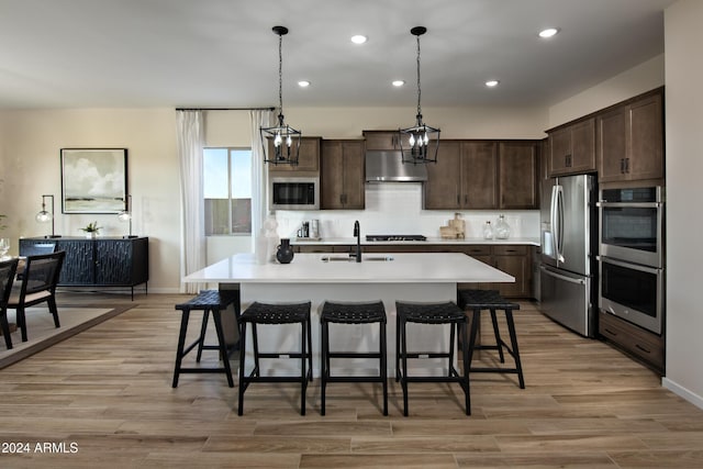 kitchen featuring sink, hanging light fixtures, stainless steel appliances, light hardwood / wood-style floors, and a kitchen island with sink