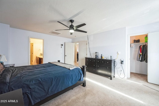 bedroom with a closet, a spacious closet, connected bathroom, ceiling fan, and light colored carpet