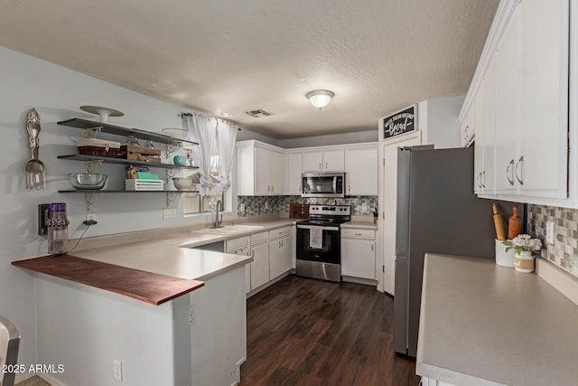 kitchen featuring a peninsula, white cabinetry, decorative backsplash, stainless steel appliances, and a sink