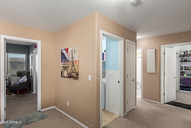 corridor with a textured ceiling, light colored carpet, and baseboards