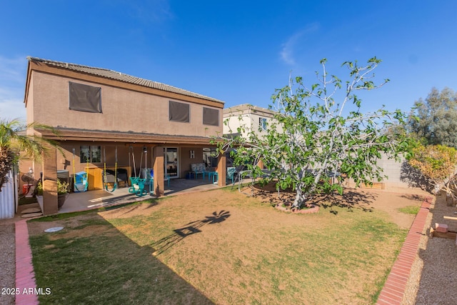 rear view of house with a patio, stucco siding, and a lawn