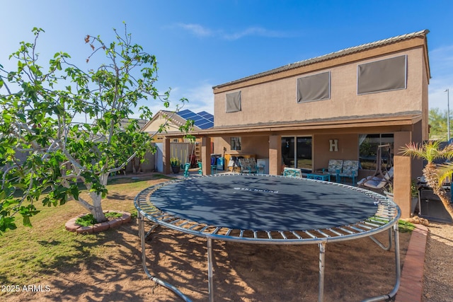 rear view of property featuring a trampoline, a patio area, and stucco siding