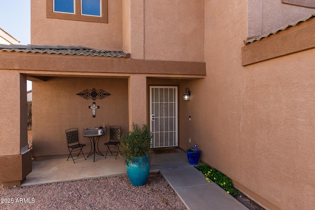 view of exterior entry featuring a patio area, stucco siding, and a tile roof