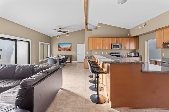 kitchen with appliances with stainless steel finishes, a ceiling fan, open floor plan, dark stone counters, and high vaulted ceiling