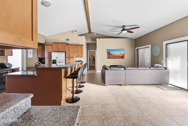 kitchen with stainless steel refrigerator with ice dispenser, a ceiling fan, a kitchen breakfast bar, light tile patterned floors, and a kitchen island