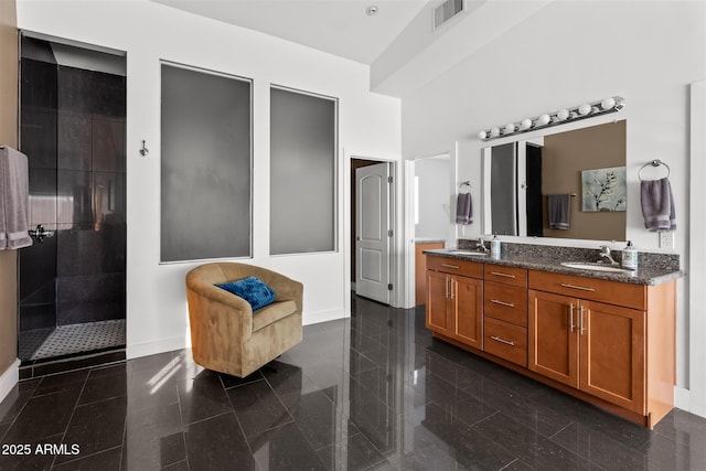 full bath with granite tiled floors, baseboards, double vanity, and a tile shower