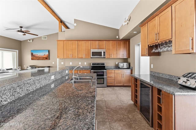 kitchen featuring appliances with stainless steel finishes, a sink, beverage cooler, ceiling fan, and dark stone counters