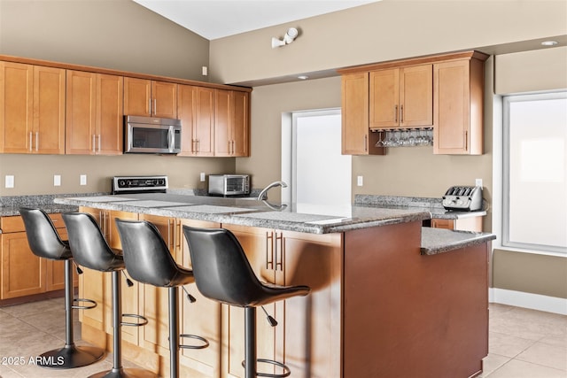 kitchen featuring stainless steel microwave, light tile patterned floors, a kitchen bar, and baseboards