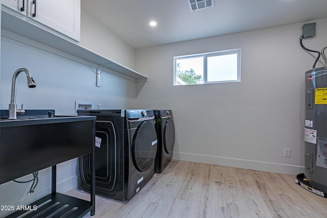 clothes washing area featuring cabinets, washing machine and dryer, electric water heater, and light hardwood / wood-style flooring