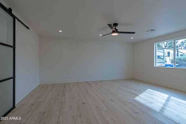 unfurnished room featuring ceiling fan, a barn door, and light wood-type flooring