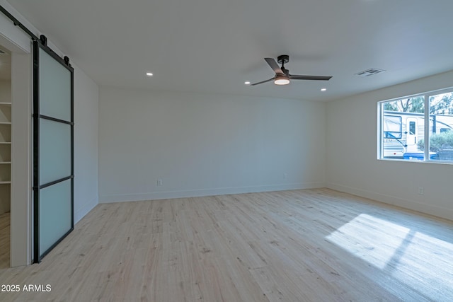 empty room featuring light hardwood / wood-style flooring, a barn door, and ceiling fan