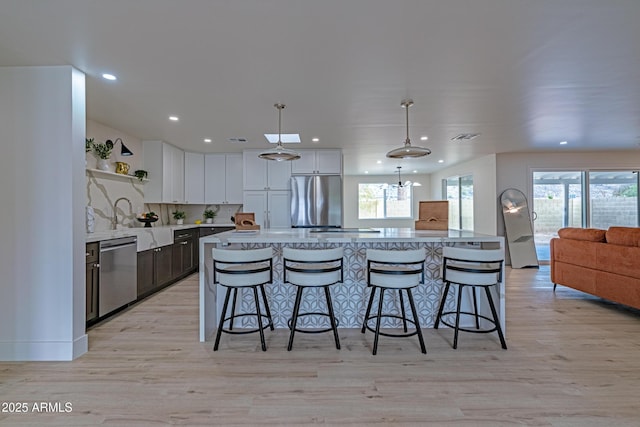 kitchen with pendant lighting, white cabinetry, a center island, stainless steel appliances, and light hardwood / wood-style flooring