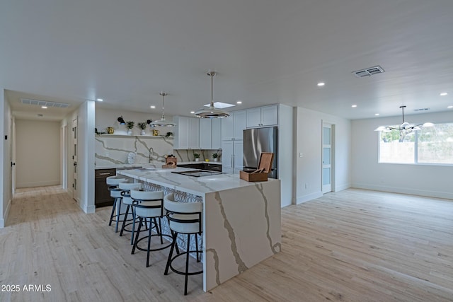 kitchen with pendant lighting, white cabinetry, stainless steel fridge, light stone counters, and a spacious island