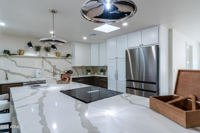 kitchen with white cabinetry, light stone counters, decorative light fixtures, and stainless steel refrigerator