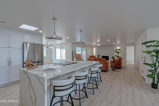 kitchen featuring white cabinetry, a brick fireplace, stainless steel refrigerator, pendant lighting, and light stone countertops