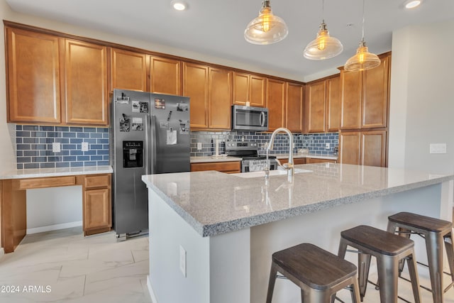 kitchen with appliances with stainless steel finishes, light stone counters, sink, decorative light fixtures, and a breakfast bar area