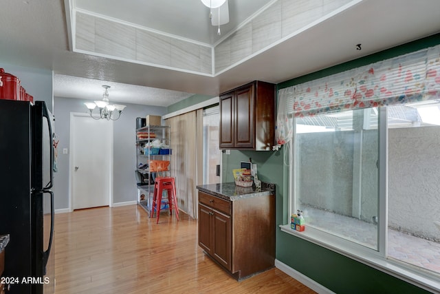 kitchen featuring black fridge, dark stone counters, light hardwood / wood-style floors, a textured ceiling, and ceiling fan with notable chandelier