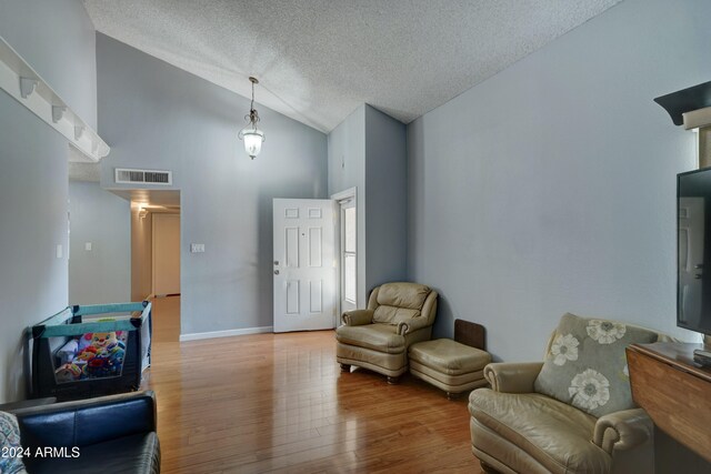 sitting room with a textured ceiling, hardwood / wood-style flooring, and high vaulted ceiling